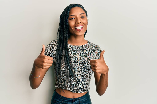 Afroamerikanerin in lässiger Kleidung Erfolgszeichen tut positive Geste mit der Hand, Daumen nach oben lächelnd und glücklich. Fröhlicher Ausdruck und Siegergeste.  - Foto, Bild
