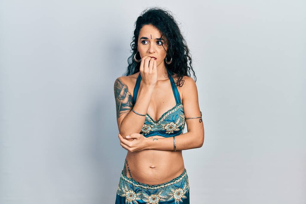 Young woman wearing bindi and traditional belly dance clothes looking stressed and nervous with hands on mouth biting nails. anxiety problem.  - Photo, Image