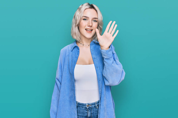 Молода блондинка в повсякденному одязі показує і вказує пальцями номер п'ять, посміхаючись впевнено і щасливо
.  - Фото, зображення