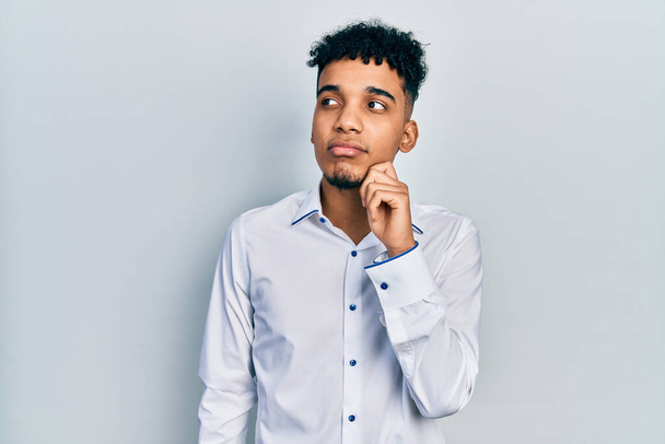Молодий афроамериканець, одягнений в ділову сорочку, думає про сумнів пальцем на підборіддя і шукає пояснення  - Фото, зображення