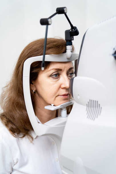 Woman has eyes examined on a slit lamp. Modern equipment for eye sigth check up in clinic. Closeup. - 写真・画像
