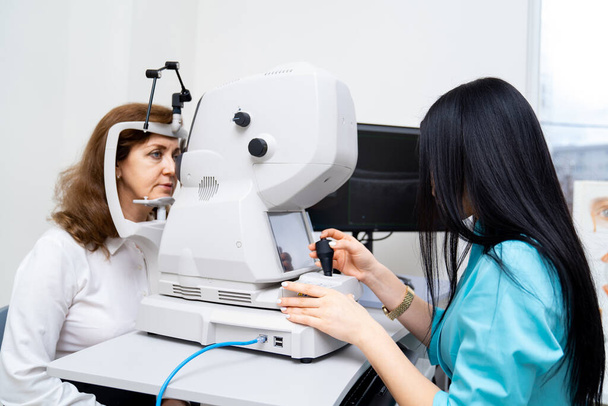 Brunette female opthometrist is diagnosing senior woman on special modern equipment. Up-to-date clinic for healthy eyes. Closeup. - Zdjęcie, obraz