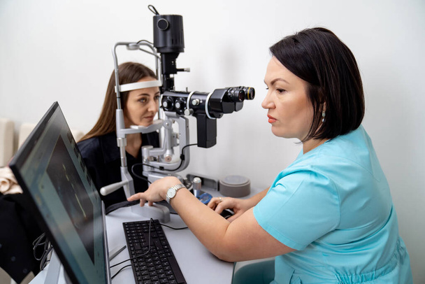 Optometry concept. Beautiful young woman is having eyes examined by an eye doctor. Experienced doctor is diagnosing female patient. Closeup. - Foto, Imagem