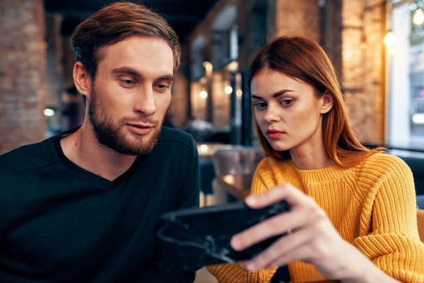 a woman in a sweater with a mobile phone and a guy with a beard are sitting in a restaurant - Photo, Image