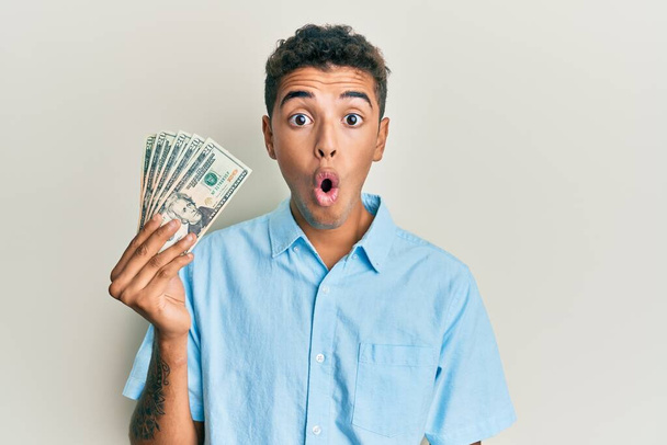 Fiatal jóképű afro-amerikai férfi kezében 20 dollár bankjegyek ijedt és csodálkozott nyitott szájjal meglepetés, hitetlen arc  - Fotó, kép