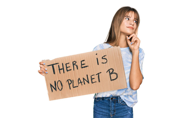 Teenager caucasian girl holding there is no planet b banner serious face thinking about question with hand on chin, thoughtful about confusing idea  - Photo, Image