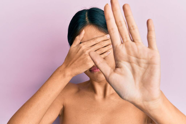 若い中国人女性は手で目を覆い、悲しいと恐怖の表情で停止ジェスチャーを行う皮膚を示すトップレス立っている。恥をかかせ否定的な概念.  - 写真・画像