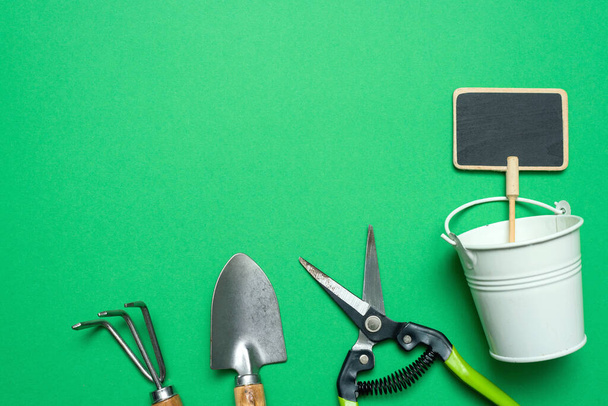 Garden tools on the green background with copy space. Rake, spade, secateurs and small water bucket. - Фото, зображення