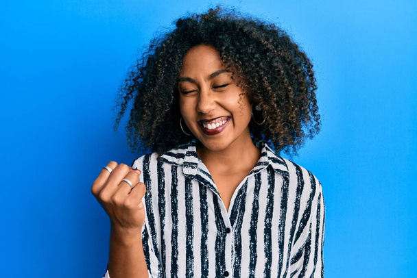 Beautiful african american woman with afro hair wearing casual clothes celebrating surprised and amazed for success with arms raised and eyes closed  - Foto, Bild