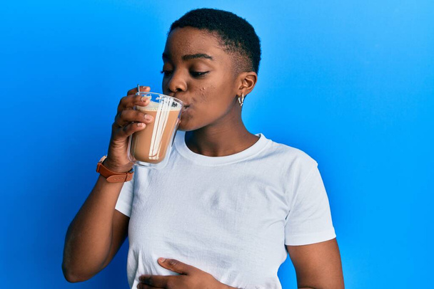 Mujer afroamericana joven bebiendo taza de café sobre fondo azul aislado - Foto, imagen