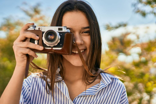 Young hispanic tourist girl smiling happy using camera at the park - 写真・画像