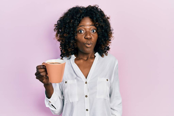 Mladá africká americká žena držící kávu vystrašená a užaslá s otevřenými ústy pro překvapení, nevěřící tvář  - Fotografie, Obrázek