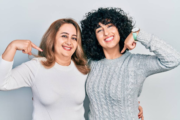 Mutter und Tochter im Nahen Osten sehen in lässiger Kleidung selbstbewusst und lächelnd aus, zeigen mit den Fingern stolz und glücklich.  - Foto, Bild