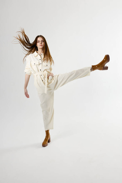 Kobieta w białych kombinezonach brązowe buty podnosi nogę w odosobnionym tle - Zdjęcie, obraz