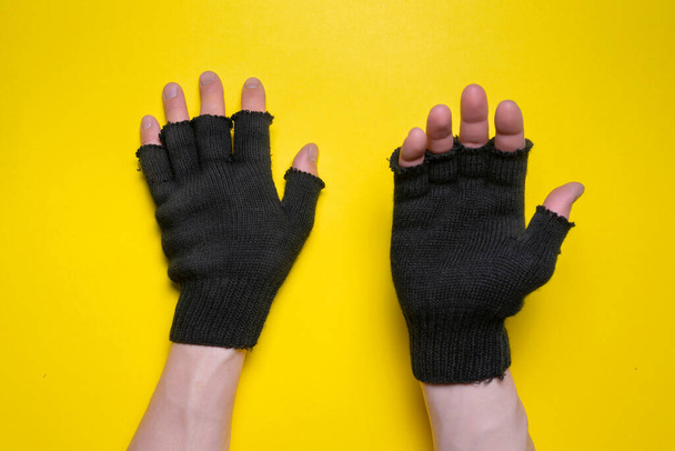 Hands in black gloves is asking for an alms isolated on the yellow background. - Foto, imagen