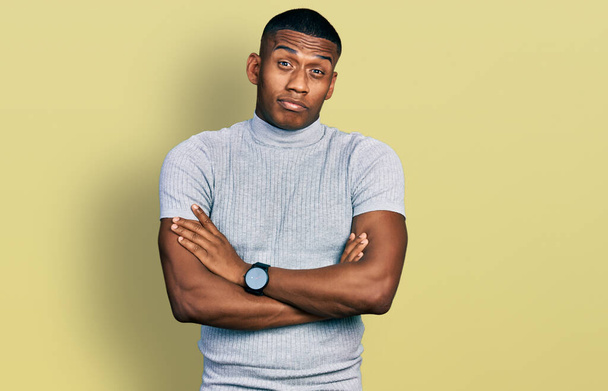 Jonge zwarte man draagt casual t-shirt sceptisch en nerveus, afkeurende uitdrukking op gezicht met gekruiste armen. negatieve persoon.  - Foto, afbeelding