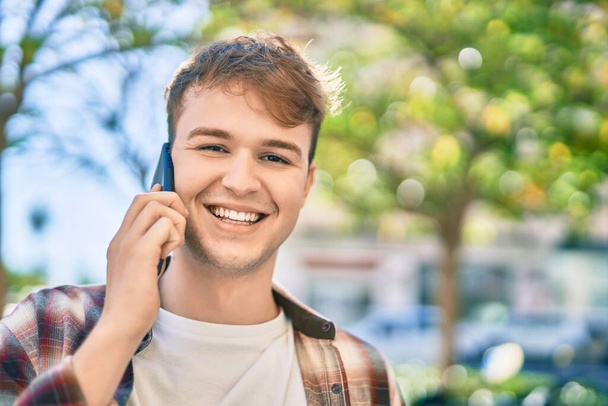 Junger kaukasischer Touristenmann lächelt glücklich und plaudert auf dem Smartphone in der Stadt. - Foto, Bild