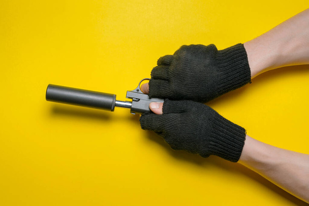 Πιστόλι παιχνιδιού με σιγαστήρα στο ανδρικό χέρι μονωμένο σε κίτρινο φόντο. - Φωτογραφία, εικόνα