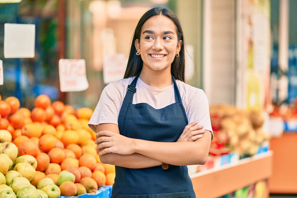 Νεαρή Λατίνα καταστηματάρχης με τα χέρια σταυρωμένα χαμογελώντας ευτυχισμένη στο κατάστημα φρούτων. - Φωτογραφία, εικόνα