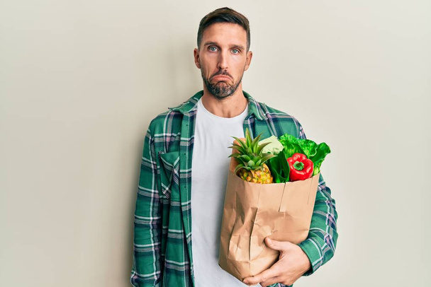 Handsome man with beard holding paper bag with groceries depressed and worry for distress, crying angry and afraid. sad expression.  - Fotoğraf, Görsel