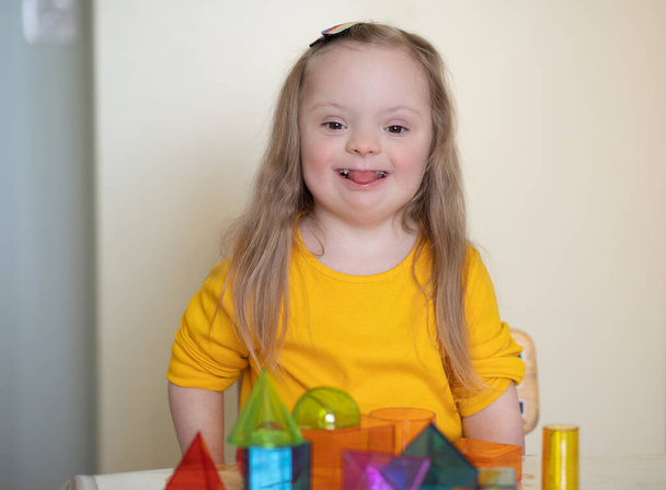Uma menina bonita com síndrome de Down brinca com um construtor, figuras transparentes brilhantes, desenvolvimento precoce da criança com deficiência. - Foto, Imagem