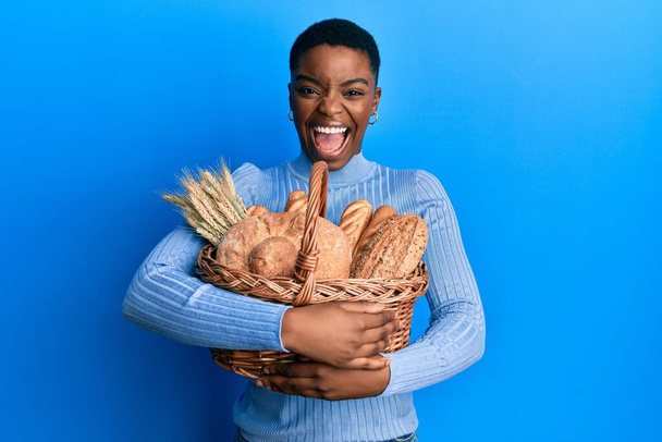 Fiatal afro-amerikai nő kezében fonott kosár kenyérrel ünnepli őrült és csodálkozott a siker nyitott szemmel sikoltozó izgatott.  - Fotó, kép