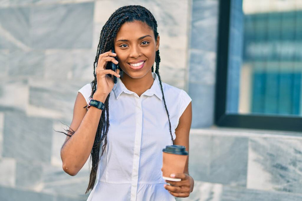 Nuori afrikkalainen amerikkalainen nainen puhuu älypuhelimella ja juo ottaa pois kahvia kaupungin. - Valokuva, kuva