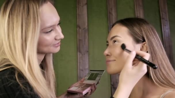 attractive caucasian makeup artist doing makeup for asian female in beauty salon - Footage, Video