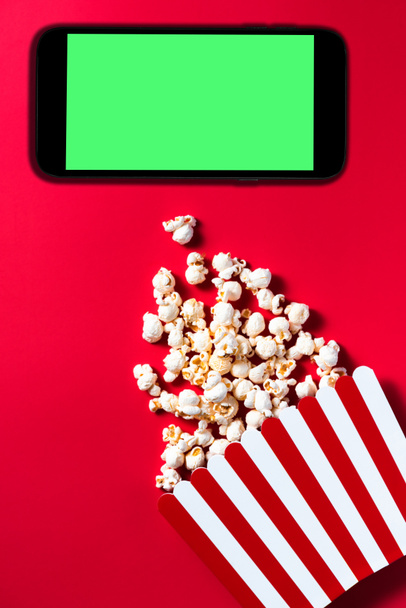 Popcorn Striped Cinema Box on Red Background. Smartphone with Green Screen Mockup Template. Flat Lay Ddesign. Digital Content Streaming Platforms. - Photo, Image