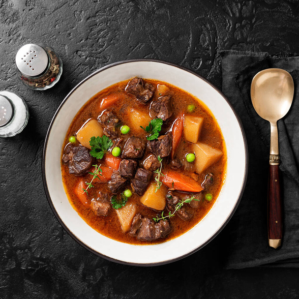 Irish stew made with beef, potatoes, carrots and herbs. Traditional St patrick's day dish. Black background, top view. - Photo, Image
