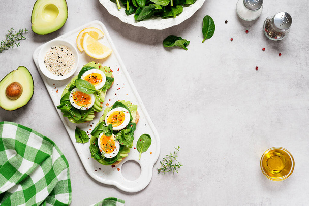 Healthy toast with sliced avocado, boiled eggs, spices and fresh spinach. Delicious breakfast or snack on gray stone background. top view, space for text - Photo, Image