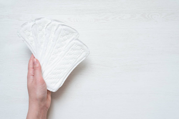 Woman is showing a daily feminine pads in her hand on the white wooden table background. - Foto, imagen