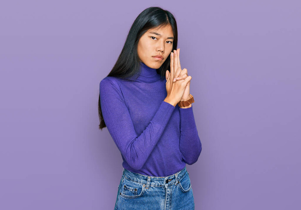 Beautiful young asian woman wearing casual clothes holding symbolic gun with hand gesture, playing killing shooting weapons, angry face  - Foto, imagen