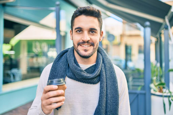 Jonge Spaanse man glimlachend gelukkig drinken af te nemen koffie in de stad. - Foto, afbeelding