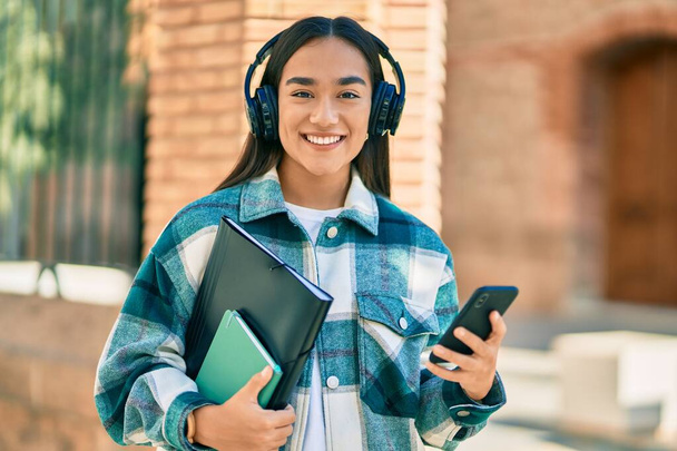 Young latin student girl smiling happy using smartphone and headphones at the city. - Foto, imagen