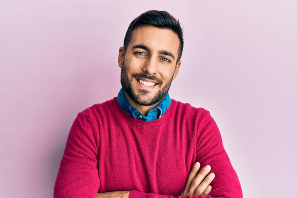 Jonge Spaanse man in casual kleding vrolijk gezicht glimlachend met gekruiste armen kijkend naar de camera. positieve persoon.  - Foto, afbeelding