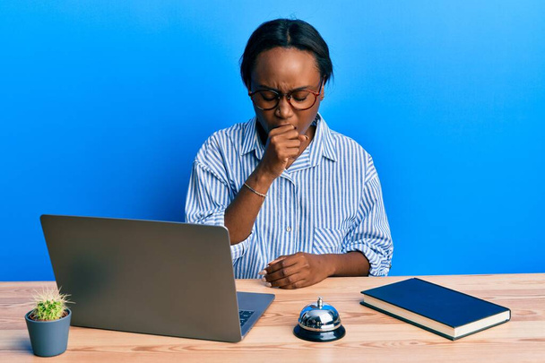 Jonge Afrikaanse vrouw die werkt bij de receptie van het hotel met behulp van laptop zich onwel voelen en hoesten als symptoom voor verkoudheid of bronchitis. Gezondheidszorgconcept.  - Foto, afbeelding