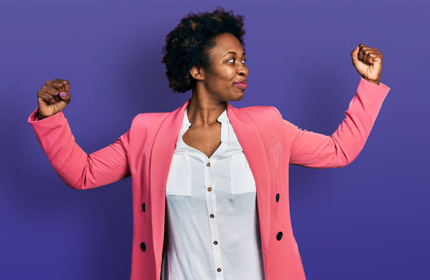 Africano mulher americana com cabelo afro vestindo jaqueta de negócios mostrando músculos braços sorrindo orgulhoso. conceito de aptidão.  - Foto, Imagem