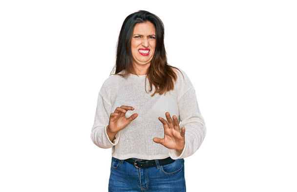 Schöne hispanische Frau in lässigem Pullover angewiderte Miene, ungehalten und ängstlich dabei Ekel Gesicht, weil Abneigung Reaktion. mit erhobenen Händen  - Foto, Bild
