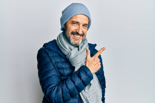 Middle age hispanic man wearing winter style smiling cheerful pointing with hand and finger up to the side  - Photo, Image