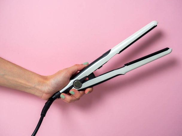 White curling iron in a woman's hand on a pnk background. An accessory for creating hairstyles. Beauty and fashion. Hair care. - Photo, Image