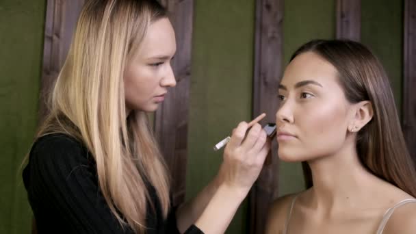 make up artist doing makeup for asian woman with eye pencil in beauty salon - Footage, Video