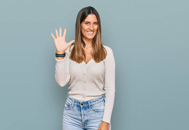 Молодая женщина в повседневной одежде показывает и указывает пальцами номер пять, улыбаясь уверенно и счастливо.  - Фото, изображение