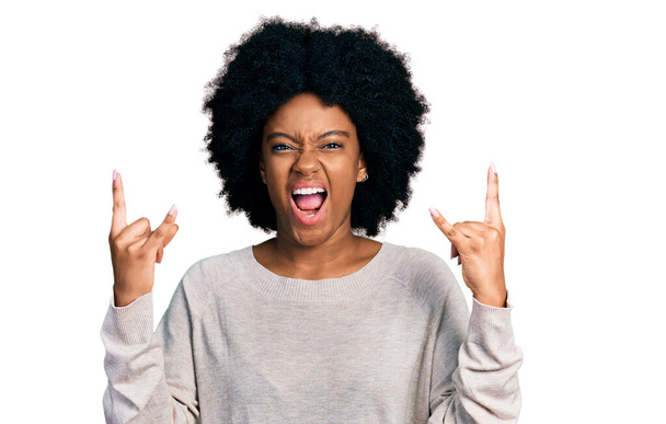 Mujer afroamericana joven con ropa casual gritando con expresión loca haciendo símbolo de roca con las manos arriba. Estrella de la música. concepto pesado.  - Foto, imagen