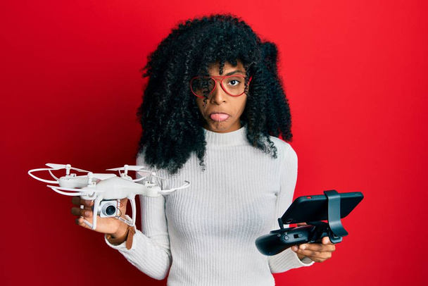 Mujer afroamericana con cabello afro usando dron con control remoto deprimida y preocupada por la angustia, llorando enojada y asustada. expresión triste.  - Foto, Imagen