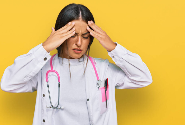 Beautiful hispanic woman wearing doctor uniform and stethoscope with hand on head for pain in head because stress. suffering migraine.  - Фото, зображення
