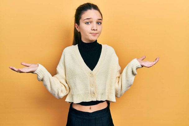 jong brunette meisje dragen casual geel jasje clueless en verward met open armen, geen idee en twijfelachtig gezicht.  - Foto, afbeelding