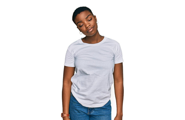 Mujer afroamericana joven que usa una camiseta blanca casual que parece somnolienta y cansada, agotada por la fatiga y la resaca, ojos perezosos en la mañana.  - Foto, Imagen