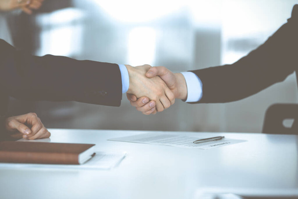 Business people shaking hands at meeting or negotiation, close-up. Group of unknown businessmen, and a woman on the background in a modern office. Teamwork, partnership and handshake concept - Foto, Imagen