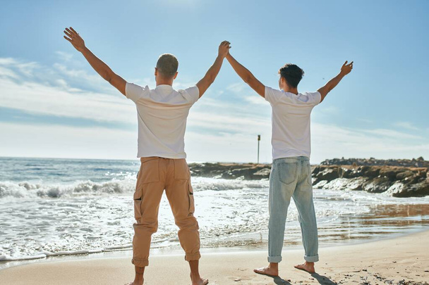 Joven pareja gay mirando al horizonte respirando en la playa. - Foto, imagen